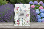 Elsie's personalised Bloom Where You Are Planted A5 floral journal standing upright on a wooden garden bench with lavender and hydrangeas in a British country garden