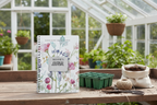 Bonnie's personalised Bloom Where You Are Planted A5 floral journal standing upright on a wooden potting bench with seed trays, compost and twine in a bright British greenhouse