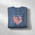 Blue crewneck sweatshirt featuring “Birthday Girl” text above a pink floral heart graphic