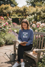 Navy sweatshirt on seated woman outdoors, 'TRYING MY BEST' quote on front