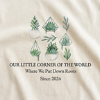 Natural t-shirt close-up with green plant graphic and “Where We Put Down Roots,” “Since 2024”