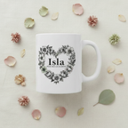 White ceramic mug with floral heart wreath and “Isla” on front