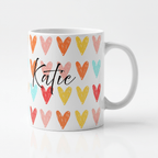 White mug with colorful heart pattern and black cursive 'Katie' on front