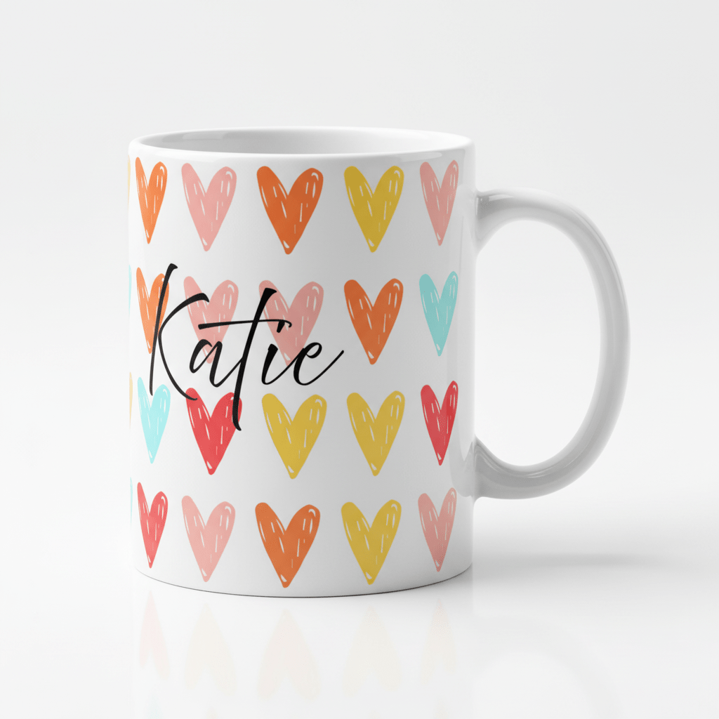 White mug with colorful heart pattern and black cursive 'Katie' on front