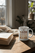 White mug with repeated KATIE lettering and heart above, with steam rising