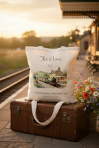 Cream canvas tote bag with illustrated train station scene and cursive family name, hanging view.