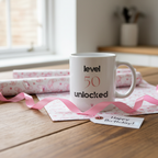 White ceramic mug on gift wrap with "level 50 unlocked" and small heart