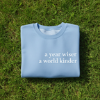 Light blue sweatshirt with “a year wiser, a world kinder.” front lettering.