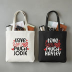 Two tote bags, one white and one black, each with printed hearts and name text