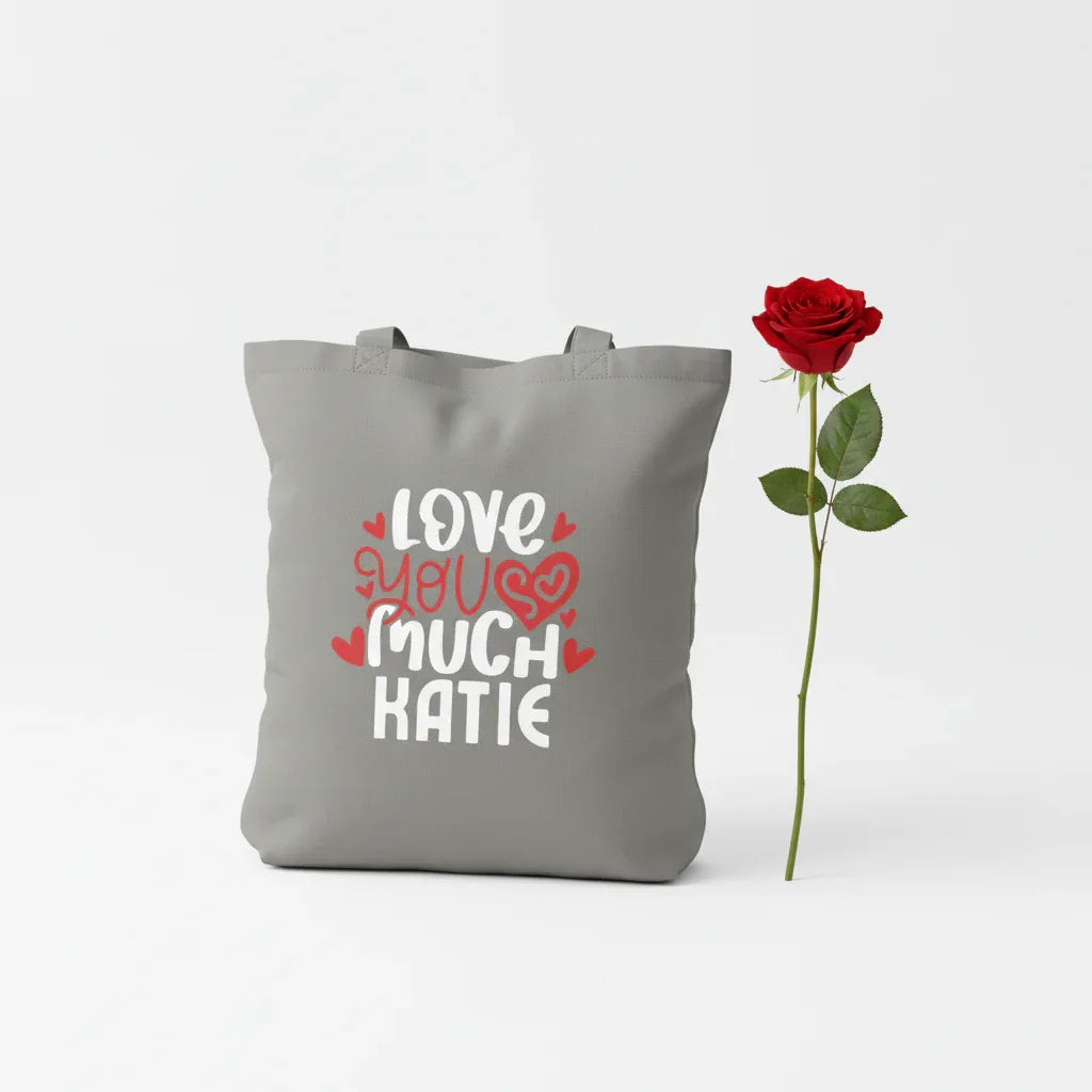 Gray tote bag with 'LOVE YOU MUCH KATIE' heart text print.