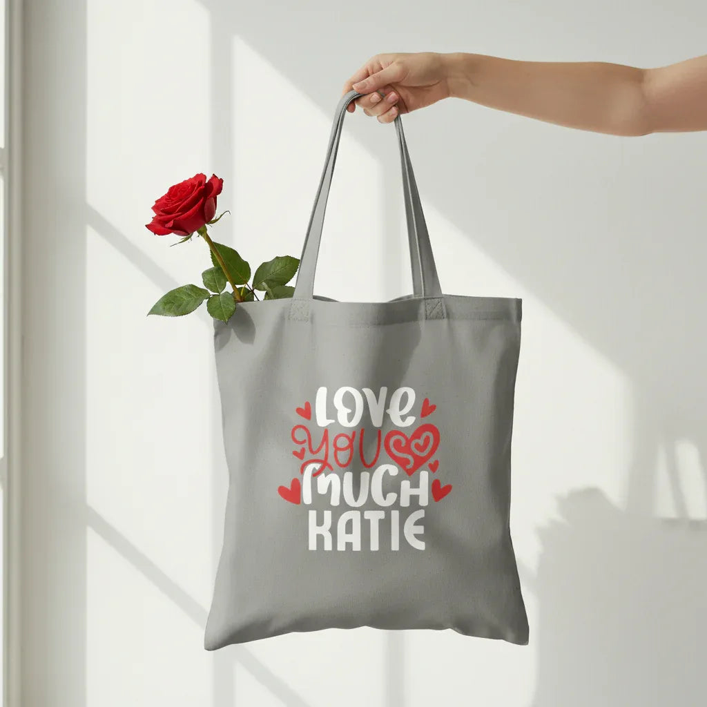 Gray tote bag with 'LOVE YOU MUCH KATIE' heart text print.