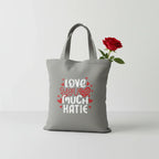 Gray tote bag with 'LOVE YOU MUCH KATIE' heart text print.