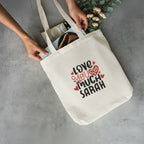 Off-white tote bag held open with printed hearts and text: “LOVE YOU MUCH SARAH”