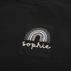 Close-up of black sweatshirt patch with embroidered rainbow arch and “sophie”