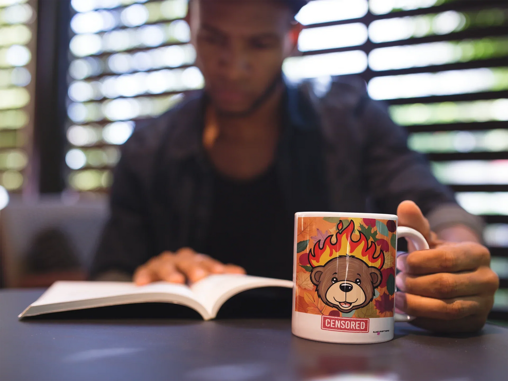 Hand holding a white ceramic bear mug with flames graphic and red “CENSORED” label.