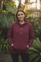 Maroon hoodie with 'delulu vibes' logo and small heart on chest, front view.