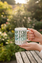 Hand holding a white ceramic mug with green MATCHA text, outdoors near plants.