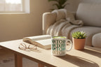 White ceramic matcha mug with green MATCHA text, on table with small plant