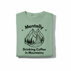 Light green T-shirt with black 'Mentally Drinking Coffee in Mountains' graphic front