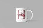 White ceramic mug with floral letter H design on front, side handle and base visible
