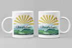 White coffee mug with sunrise rays and mountain landscape graphic on front