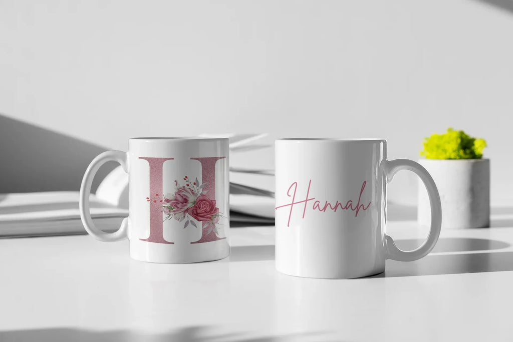 White ceramic mugs: floral letter I on one and pink cursive name Hannah on the other.