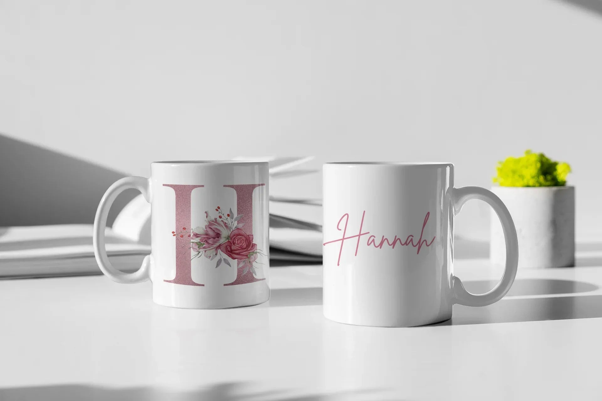 White ceramic mugs: floral letter I on one and pink cursive name Hannah on the other.