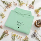 Mint green hoodie laid flat with drawstring hood and “delulu vibes” slogan
