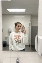 White crewneck sweatshirt with floral quote graphic, long sleeves and ribbed cuffs