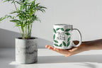 White coffee mug with green leaf wreath design and “Trust the Process” in an open hand