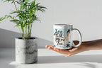 Hand holding a white tea mug with 'Less Talk, More Tea' text and stone graphic