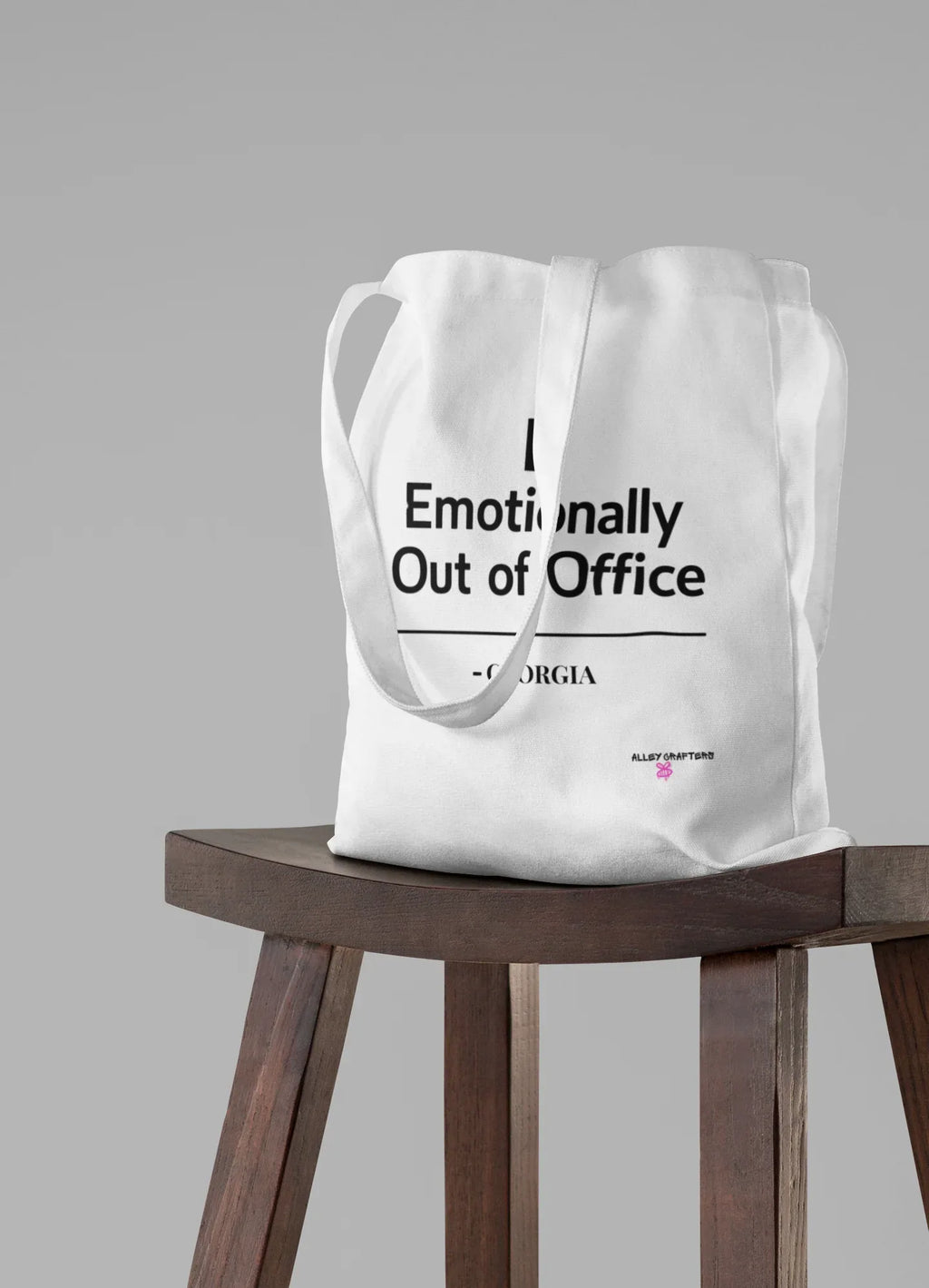 White tote bag with 'Emotionally Out of Office' slogan on front.