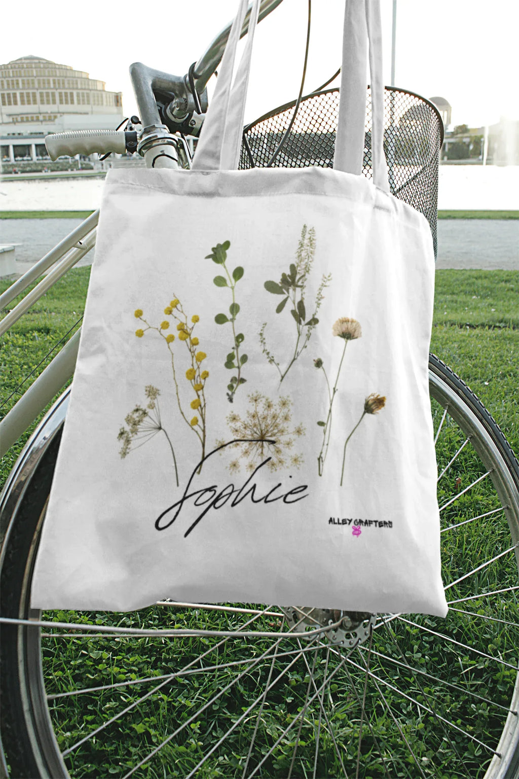 White canvas tote bag with botanical plants print and cursive logo, short handles