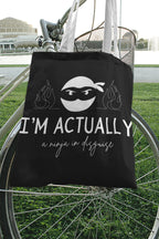 Black tote bag with ninja face graphic, 'I'M ACTUALLY', and 'a ninja in disguise'.