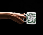 White mug with green leaves and “Trust the Process” text as a hand grips the handle