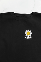 Black crewneck sweatshirt with flower smiley square patch on left chest.