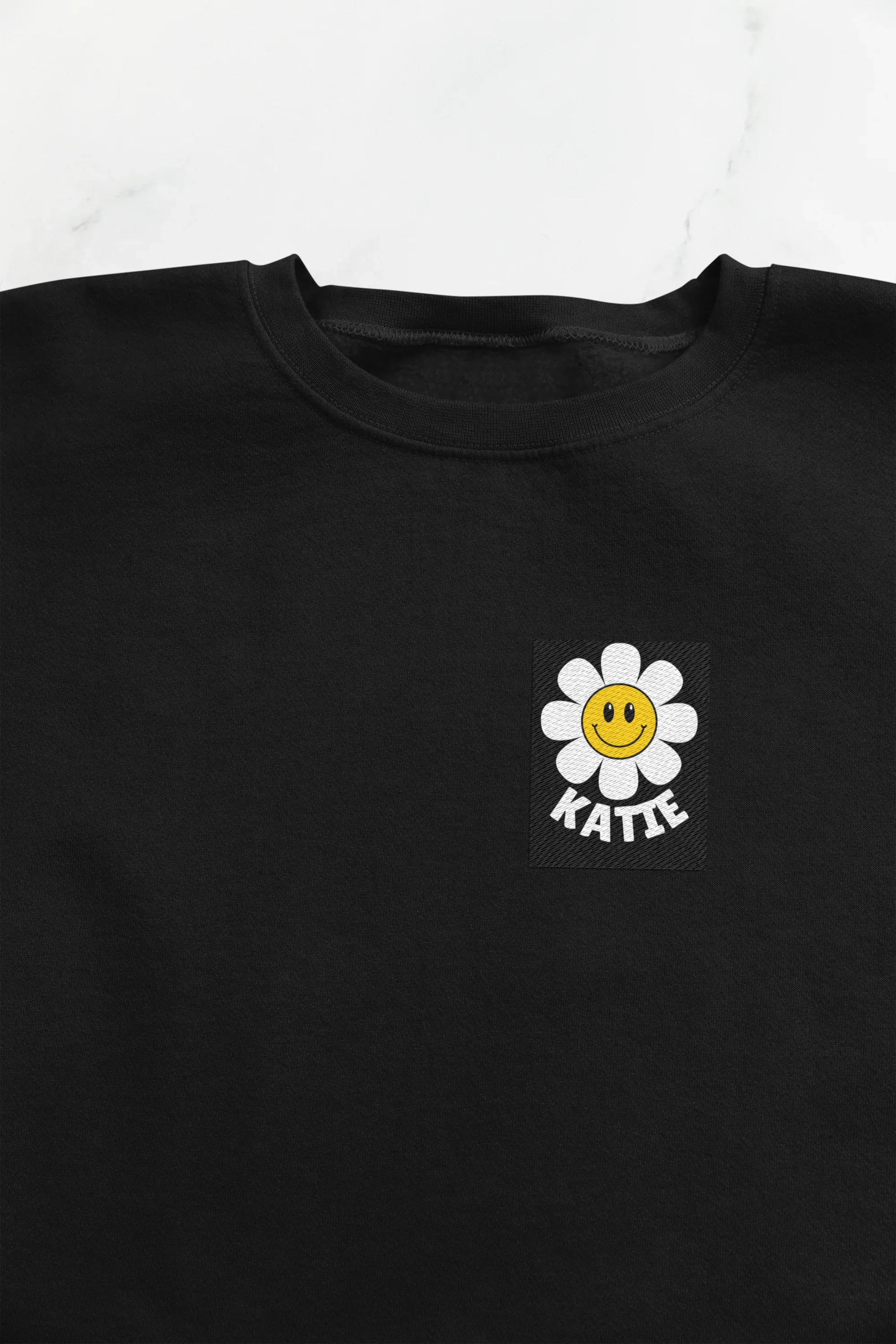 Black crewneck sweatshirt with flower smiley square patch on left chest.