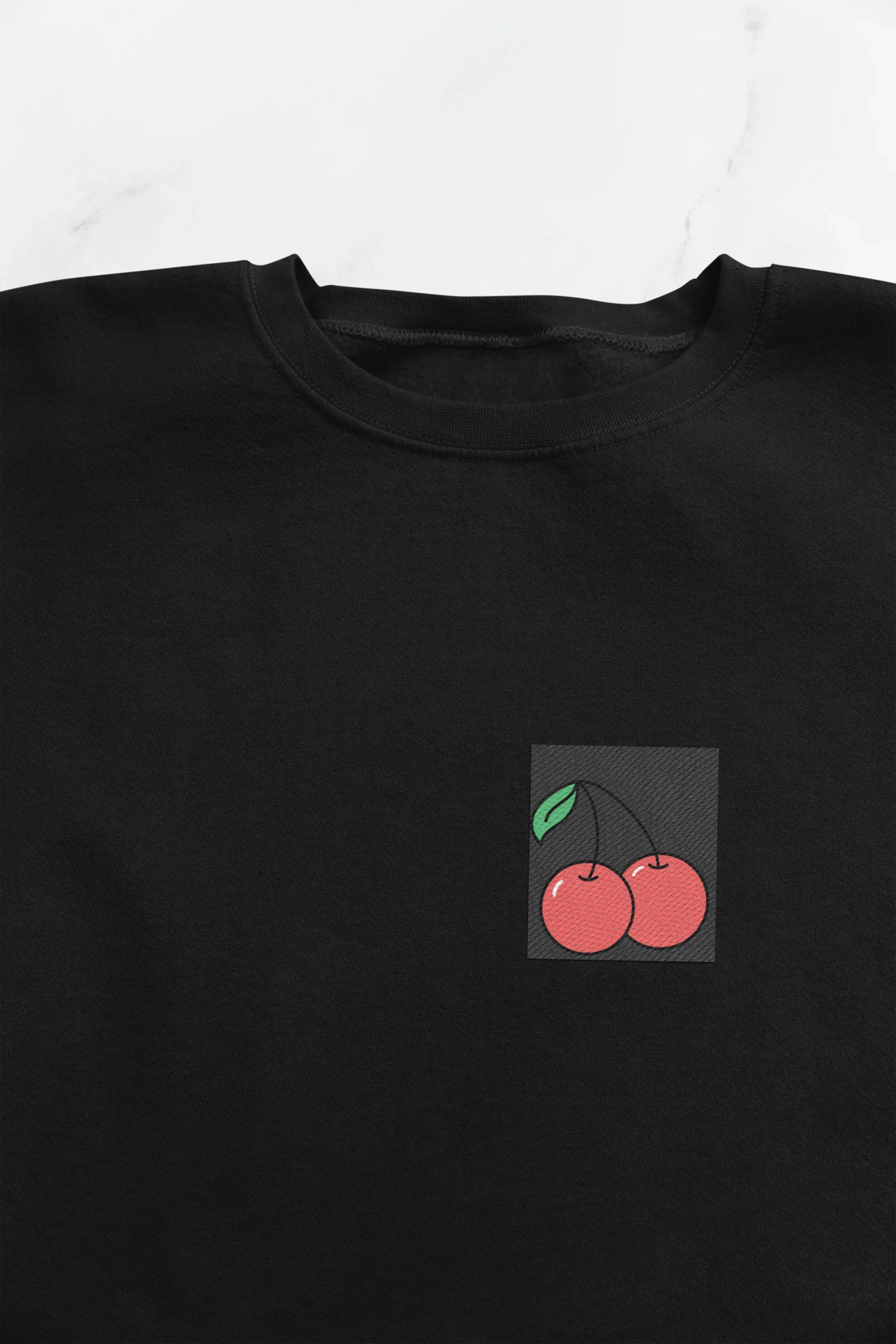 Black crewneck sweatshirt close-up with cherry embroidery patch on chest