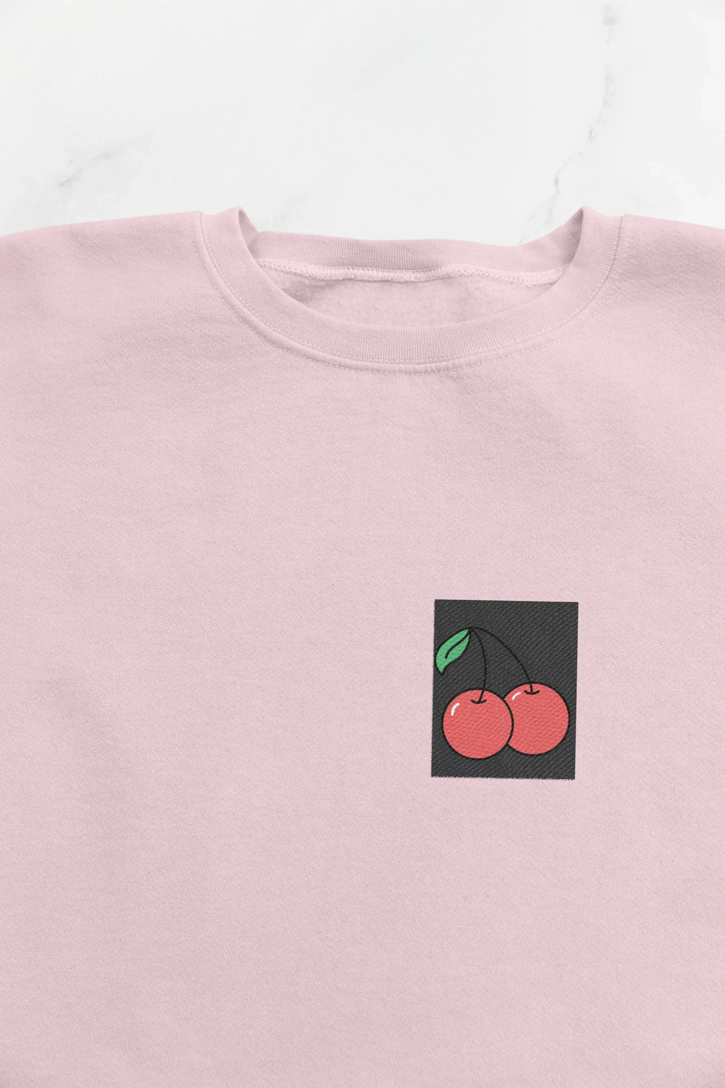 Light pink crewneck sweatshirt close-up with cherry embroidery patch on chest