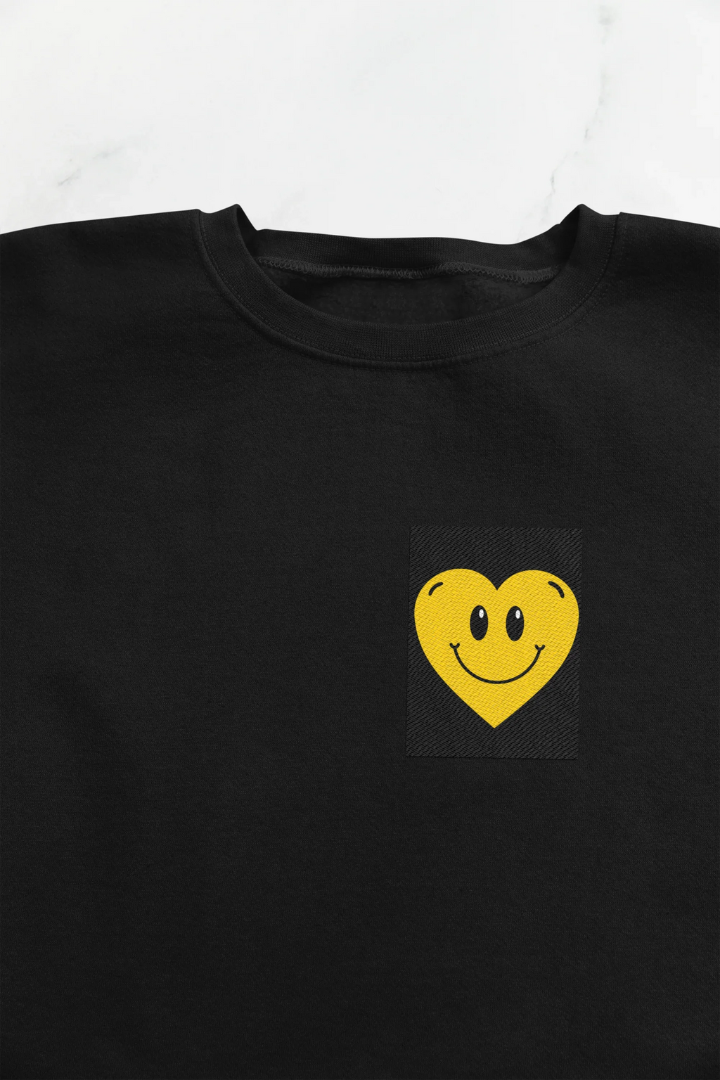 Black crewneck sweatshirt with embroidered yellow smiley heart patch on chest