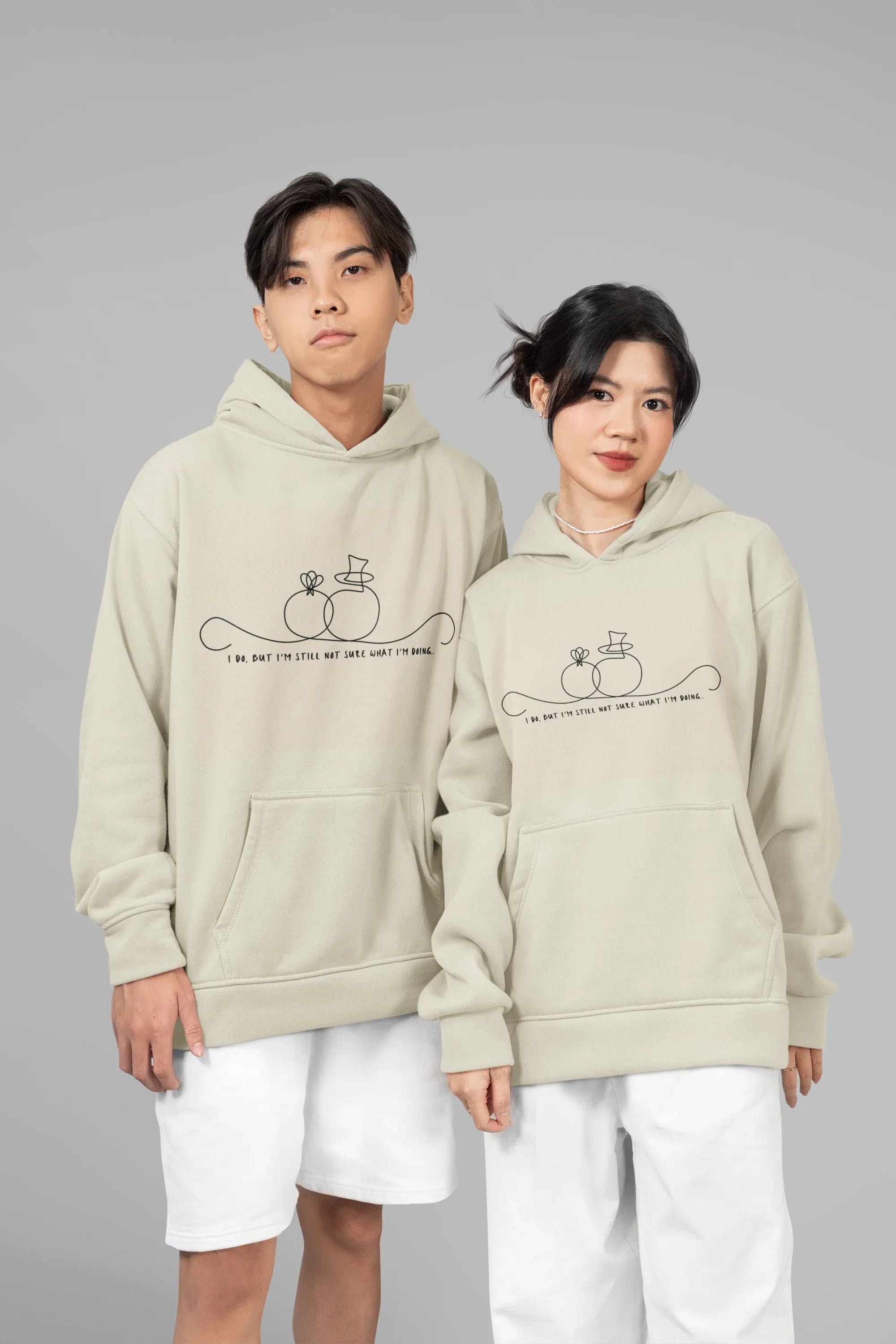 Light beige unisex hoodies worn together; front pocket and line-art wedding rings graphic.