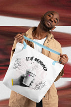 White coffee tote with light blue handles, front print of “STAY GROUNDED” and coffee mug