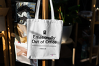 White canvas tote bag hanging with black top handles and bold front slogan text