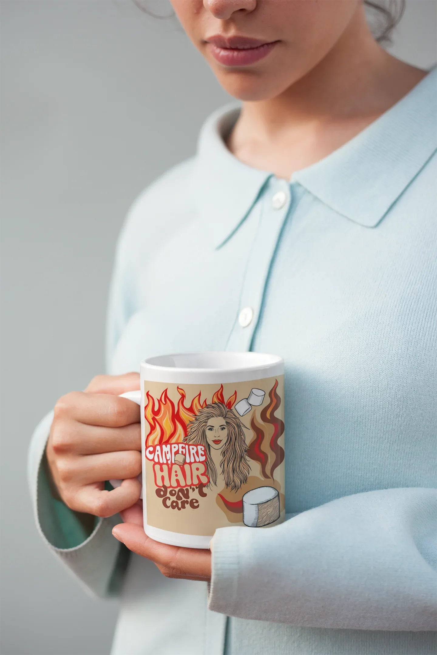 White ceramic mug in hand with flame-haired woman and campfire coffee graphic