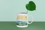 White coffee mug with sunrise landscape print and illustrated starburst on front