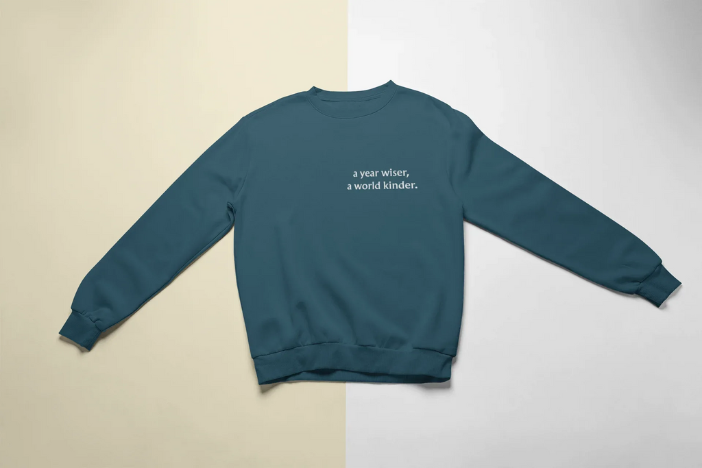 Teal crewneck sweatshirt with "a year wiser, a world kinder" text on chest