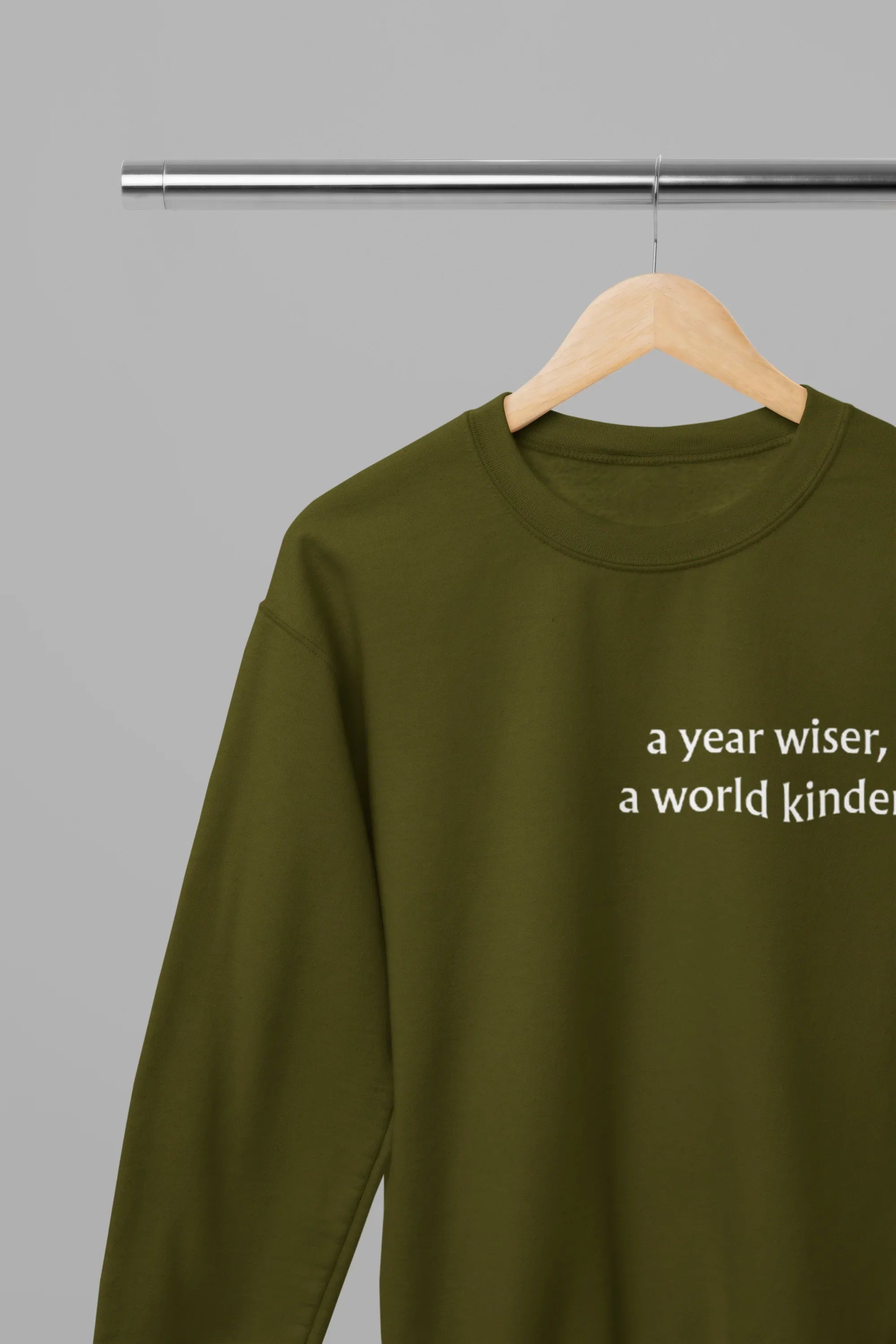 Olive green crewneck sweatshirt on hanger with "a year wiser" text detail