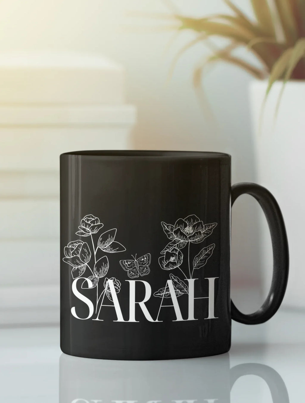 Black ceramic mug with floral line art and name SARAH on front