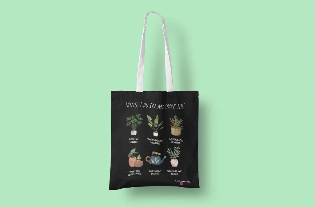 Black tote bag with white handles and plant collage artwork on the front panel.