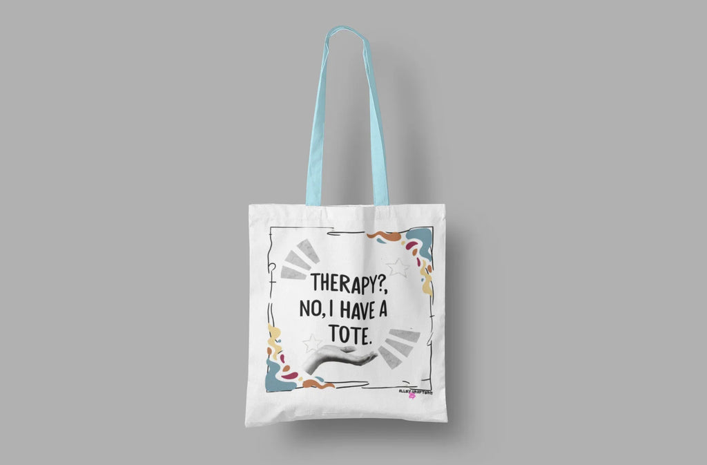Flat-lay white tote bag with blue handles, printed quote and colorful doodle border.